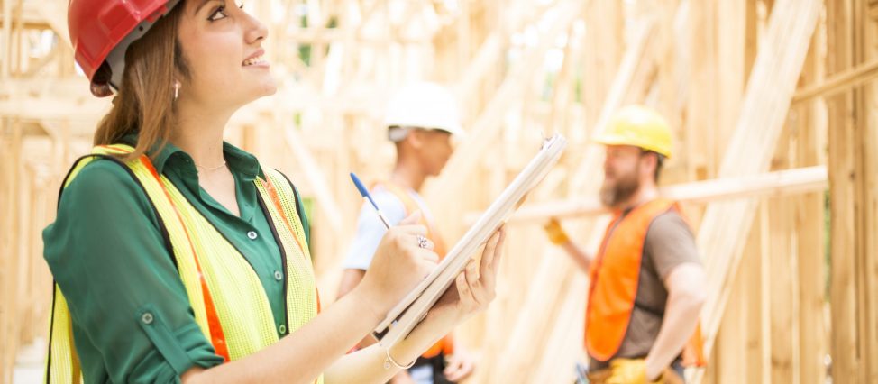 Latin descent female foreman or inspector checks blueprints in construction building site.   Other workers background.